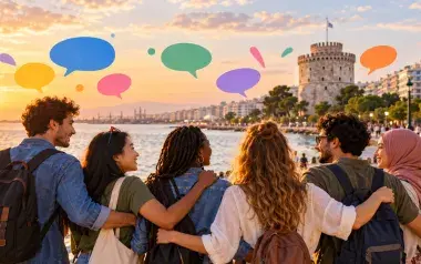Πολυπολιτισμική ομάδα νέων ανθρώπων βρίσκεται μαζί στην παραλία της Θεσσαλονίκης, με φόντο τον Λευκό Πύργο και πολύχρωμα σύμβολα διαλόγου. Η εικόνα αποδίδει το μήνυμα «Languages Unite!» της Ευρωπαϊκής Ημέρας Γλωσσών 2026 και συμβολίζει την πολυγλωσσία, την πολιτισμική ποικιλομορφία, τον σεβασμό και την επικοινωνία μεταξύ ανθρώπων διαφορετικής προέλευσης